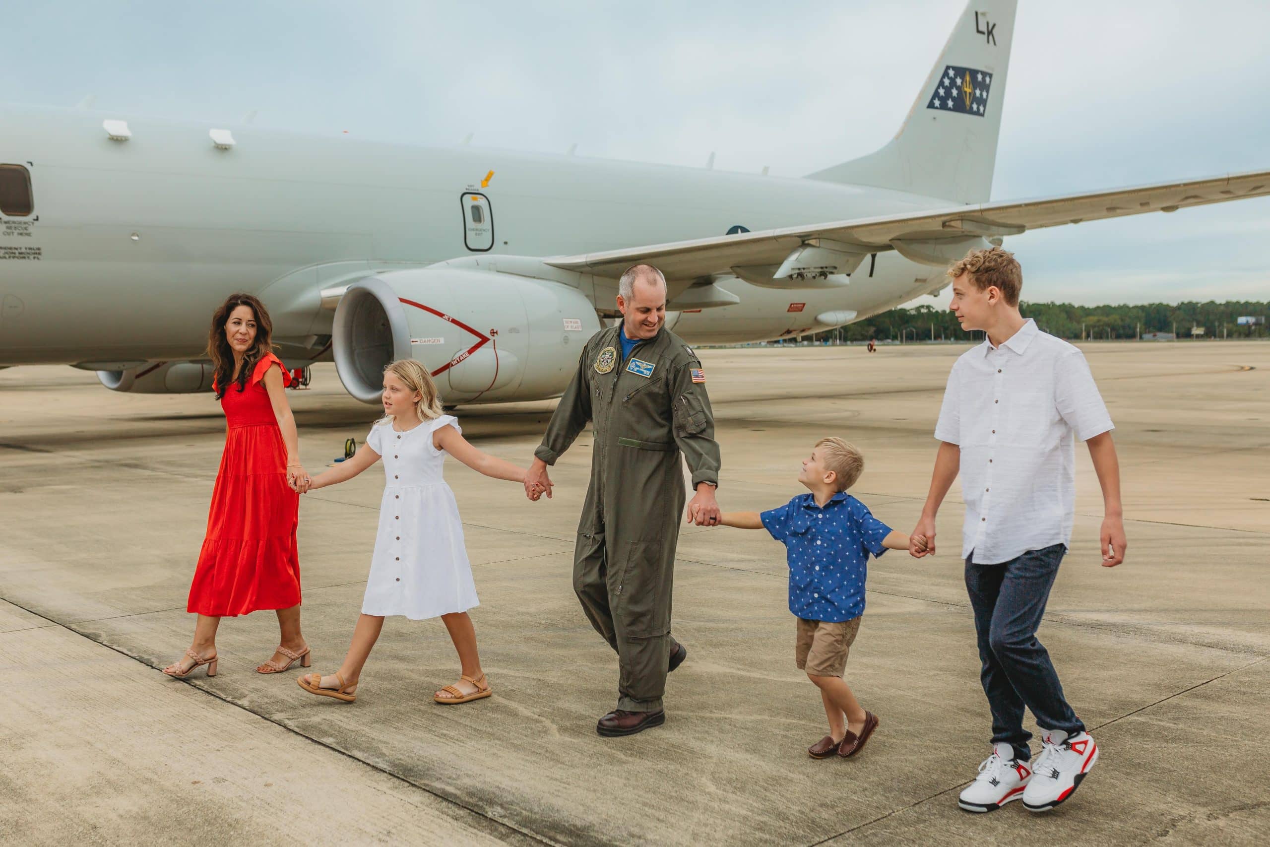 Family walking hand-in-hand on the airport tarmac beside a large white airplane.