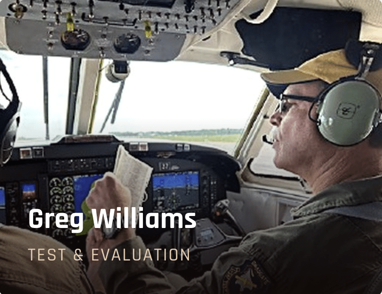 Pilot in cockpit wearing a headset, reviewing a checklist; overlay text shows 'Greg Williams' and 'Test & Evaluation'.