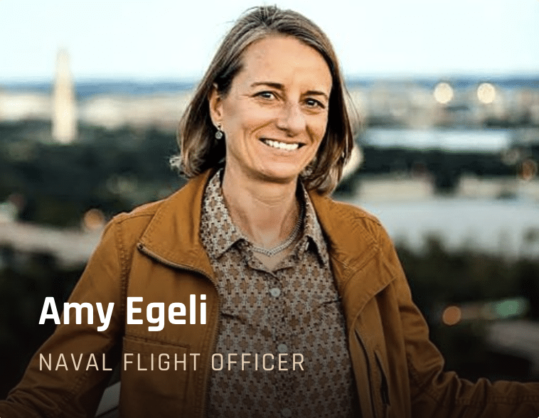 Portrait of Amy Egeli, Naval Flight Officer, smiling outdoors with a city skyline in the background.