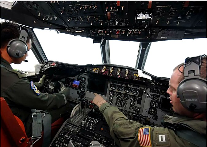 Two pilots in headsets sit in a cockpit, adjusting flight instruments and controls.